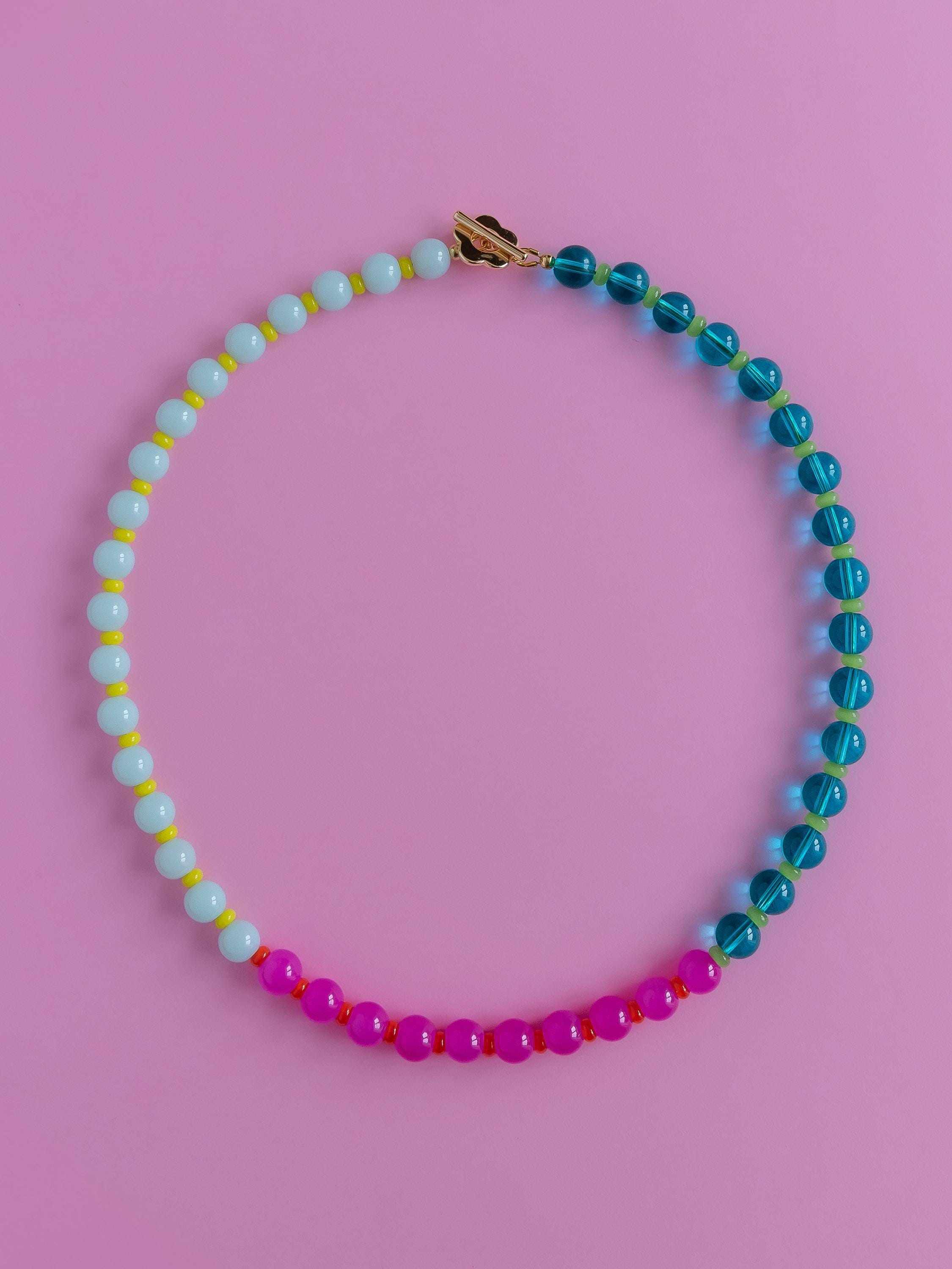 Cloudberry Cream necklace laid in a circle on a pink background, deep turquoise beads down one side, pale milky green down the other and hot pink across the bottom